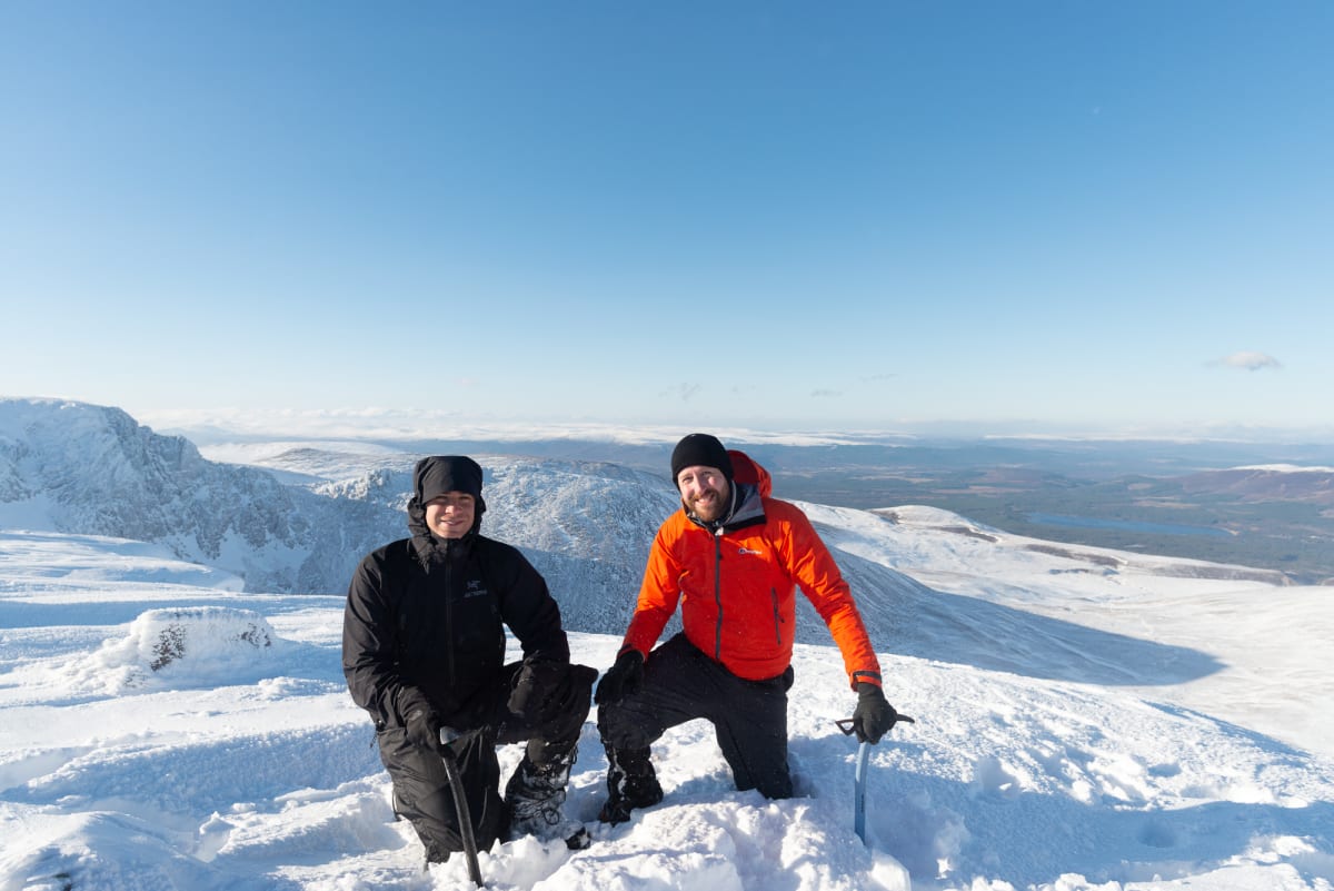Ed and Chris kneel down with ice axes in hand at the top of Stob Coire an t-Sneachda
