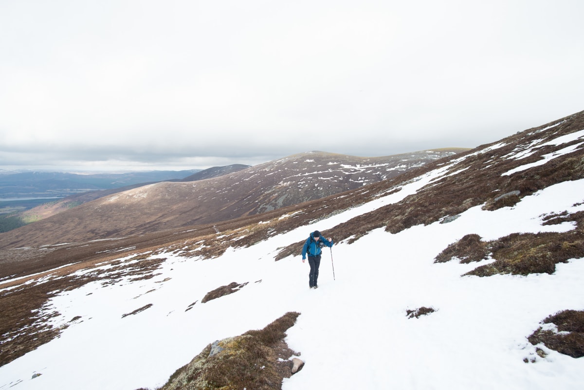 Ed hiking uphill on a partially snow covered slope.