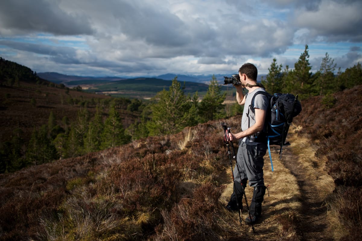 Chris taking a photo looking down a sunny hillside. There’s dark clouds in the background.