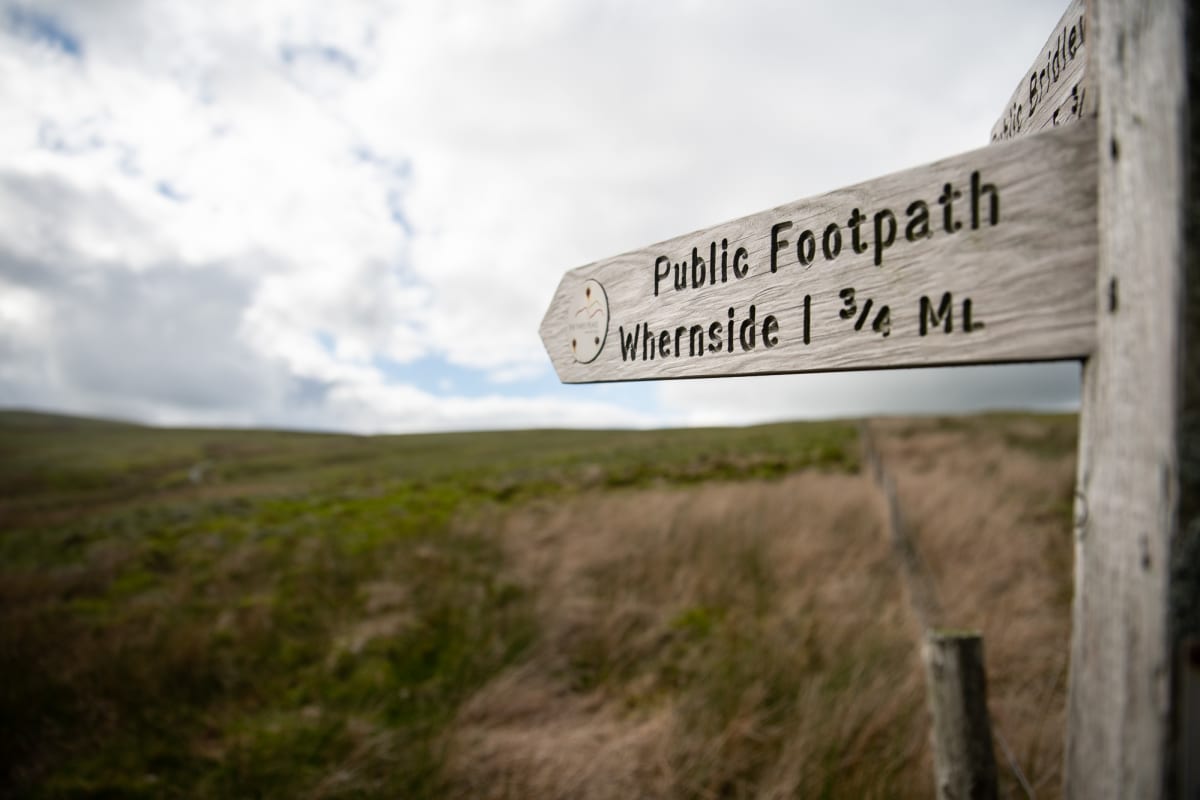 A footpath sign points from right to left, marking the summit of Whernside, 1.75 miles away.