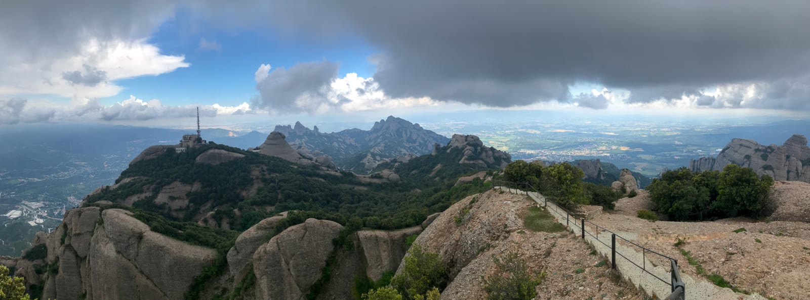 A panorama taken a the top of Sant Jeroni in Montserrat. The sky is gloomy but clear skies can be seen in the distance.