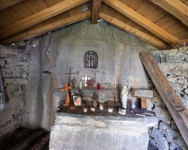 Looking inside a small chapel. The inside is bare except for a few religious artefacts on a cement table.