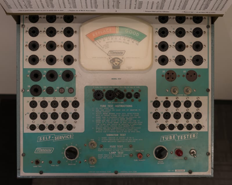 A photo of the front of a vintage ‘tube tester’. The camera is looking directly down on a control panel. There’s dials and inputs all over, with a large swinging gauge in the center.