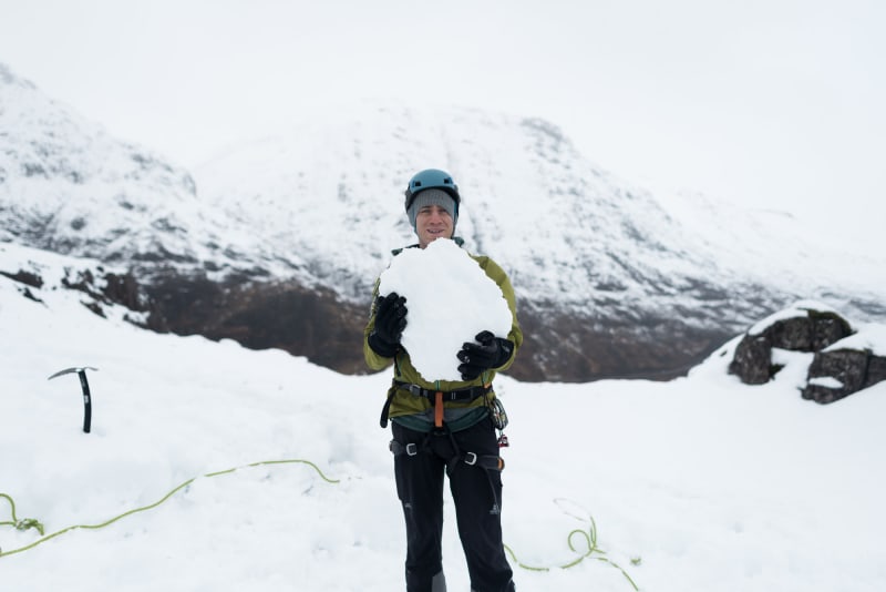 Chris holds a large boulder of snow as he faces the camera.