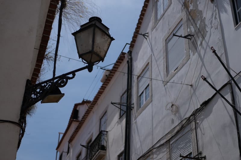 Looking up at a streetlamp in a narrow street. It’s daylight, so the streetlamp isn’t on.