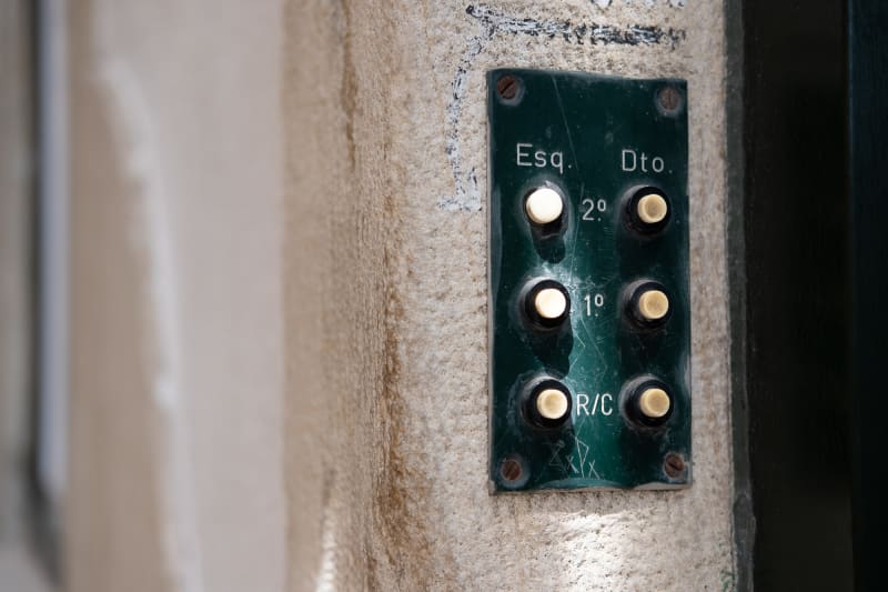 A macro photo of a set of doorbells on the wall. There are 6 white buttons on a dark green base.