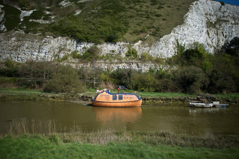 A small faded orange life raft moored on the side of the river Ouse.