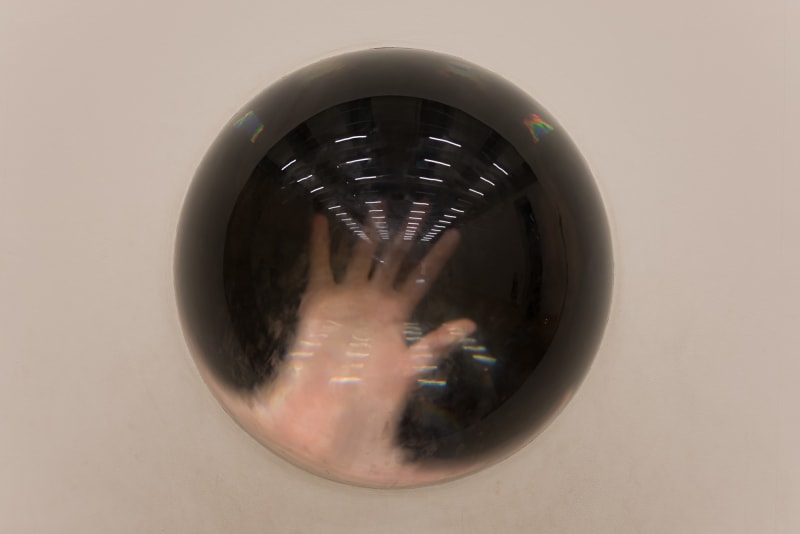 A semicircle of solid glass sits in a white wall. A hand is visible on the other side, magnified.