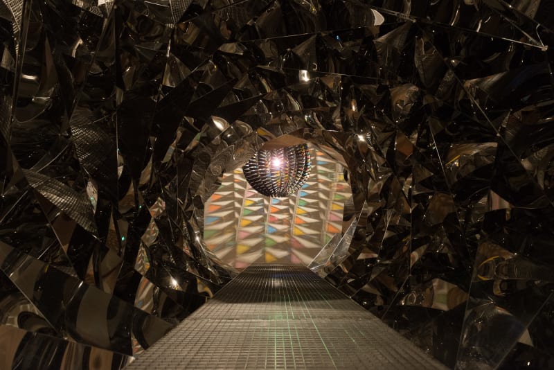 Looking down a metallic tunnel to a light fixture at the end.