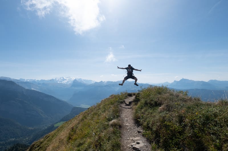 Oj in the air, mid jump. He’s high up on a mountainside in the bright sun.