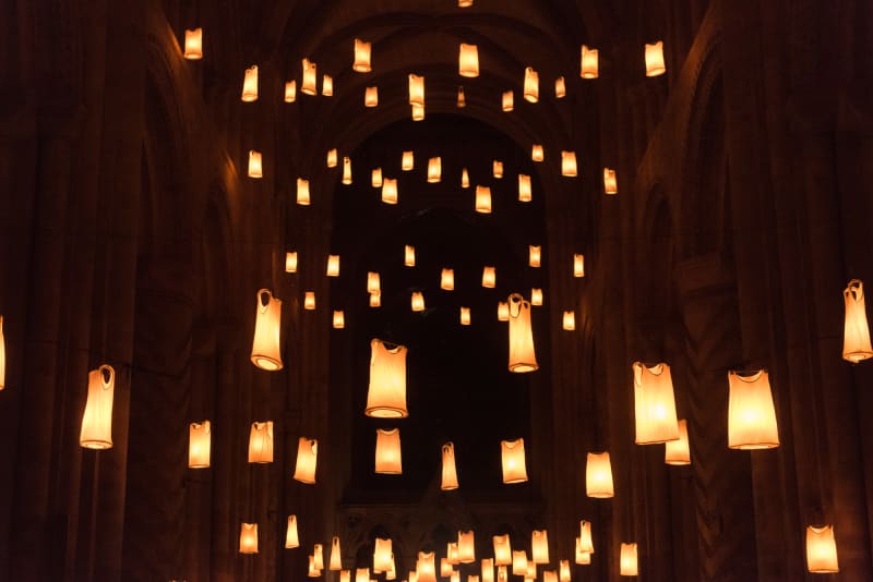 The vast hall of Durham Cathedral at night. The hall is filled at various levels by warm hanging lights. On closer inspection, the lights are made from white vests lit from within.