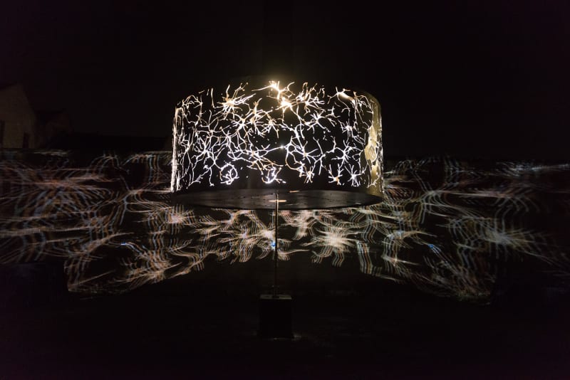 A large cylindrical light projects abstract patterns outwards on to the surrounding walls