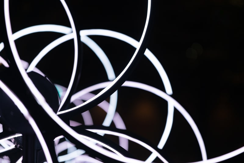 A close crop of of a lighting installation formed from many rings stacked in front of each other, with the inside of the ring light up in solid white. Seen from the front you can see many partial solid arks of white in a geometric pattern.