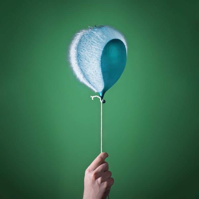 Photo of a water balloon bursting; it is attached to a string like a helium balloon.