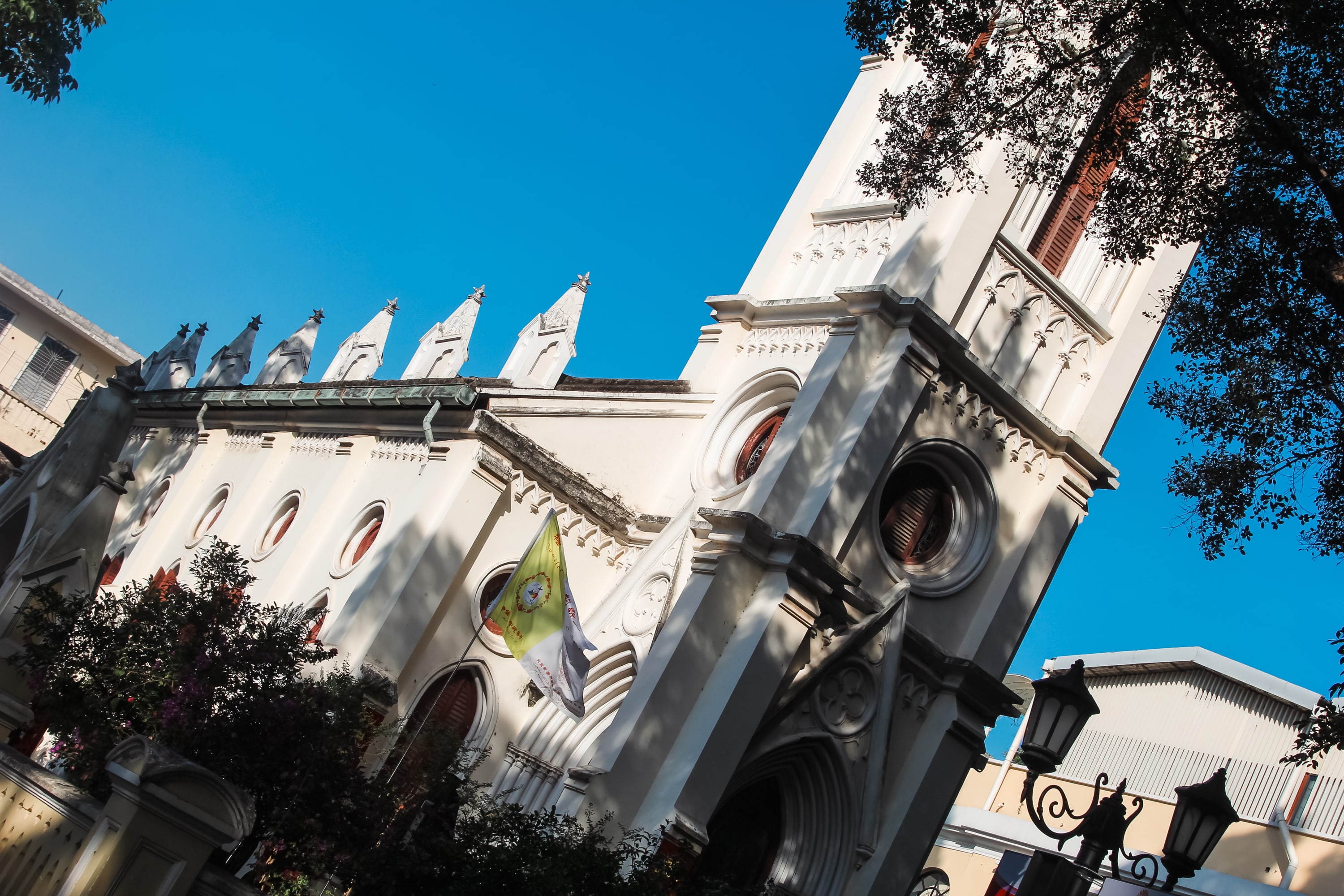 A white church with tall arched windows and a flag near the entrance is seen from a low angle, framed by trees and blue sky—a peaceful scene in gay Guangzhou, highlighting the city’s diversity and vibrant LGBTQ presence.