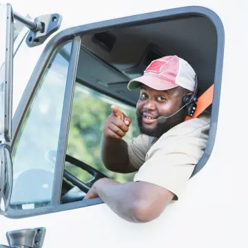 Black Male Truck Driver behind the wheel, smiling and pointing