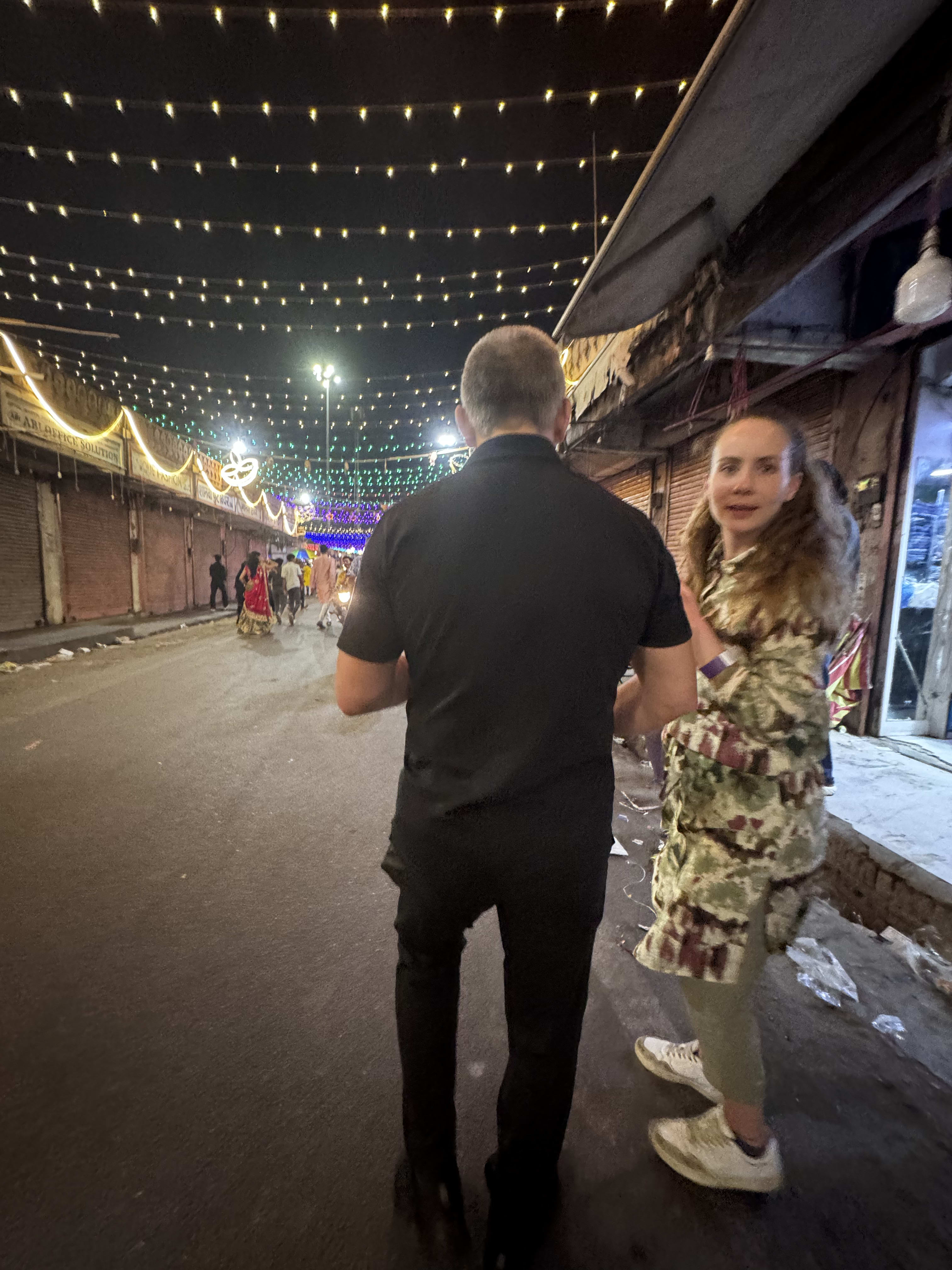 Travellers walking a market street strung with lights at night