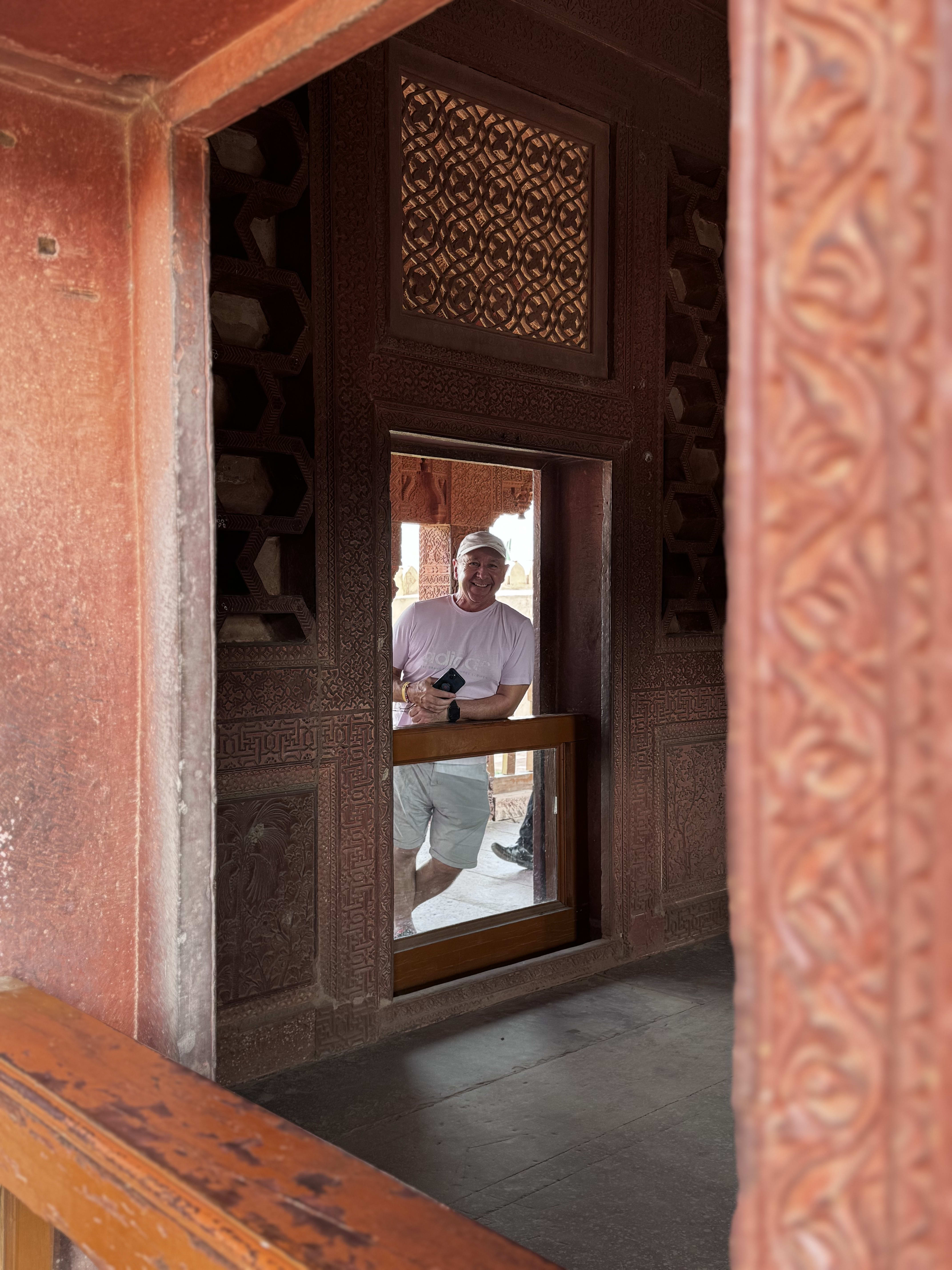 A carved red sandstone window with a visitor reflected