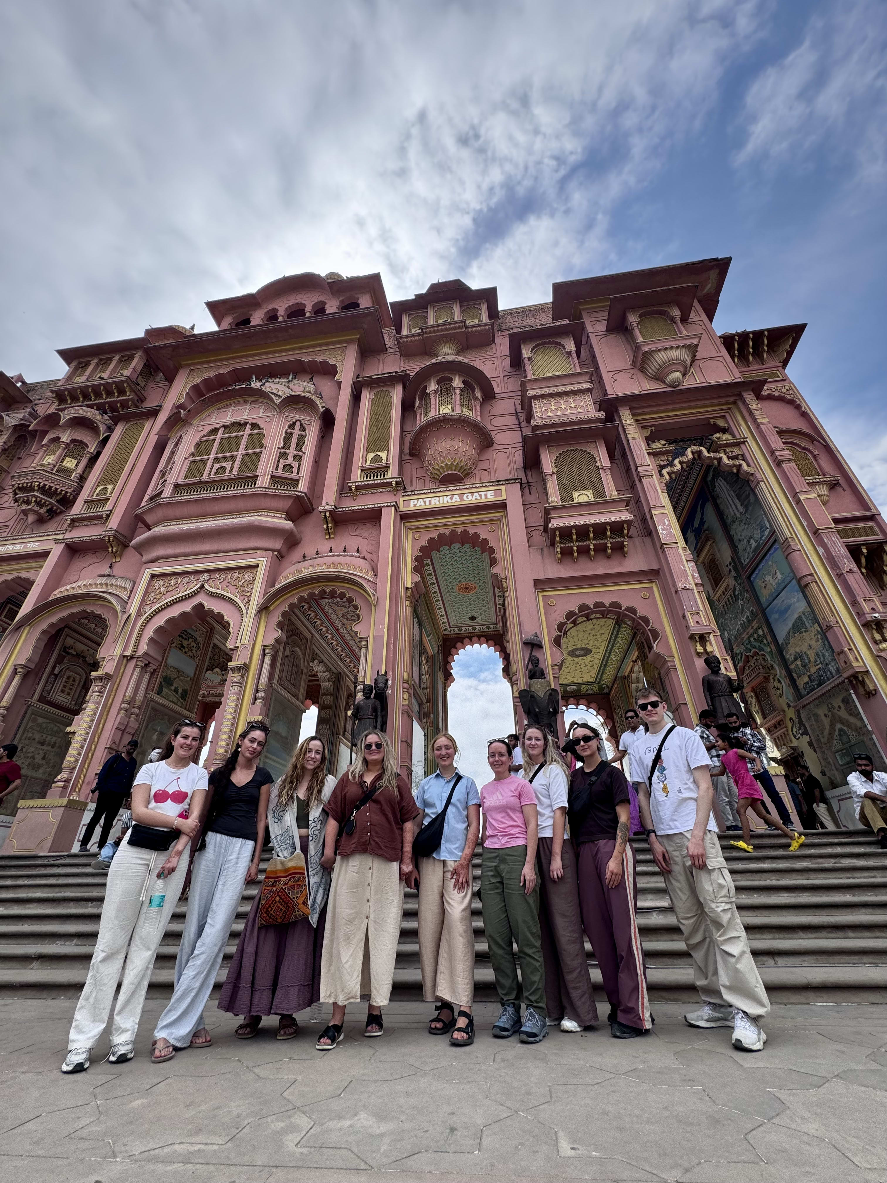 Travellers on the steps of a pink carved facade in Jaipur's old city