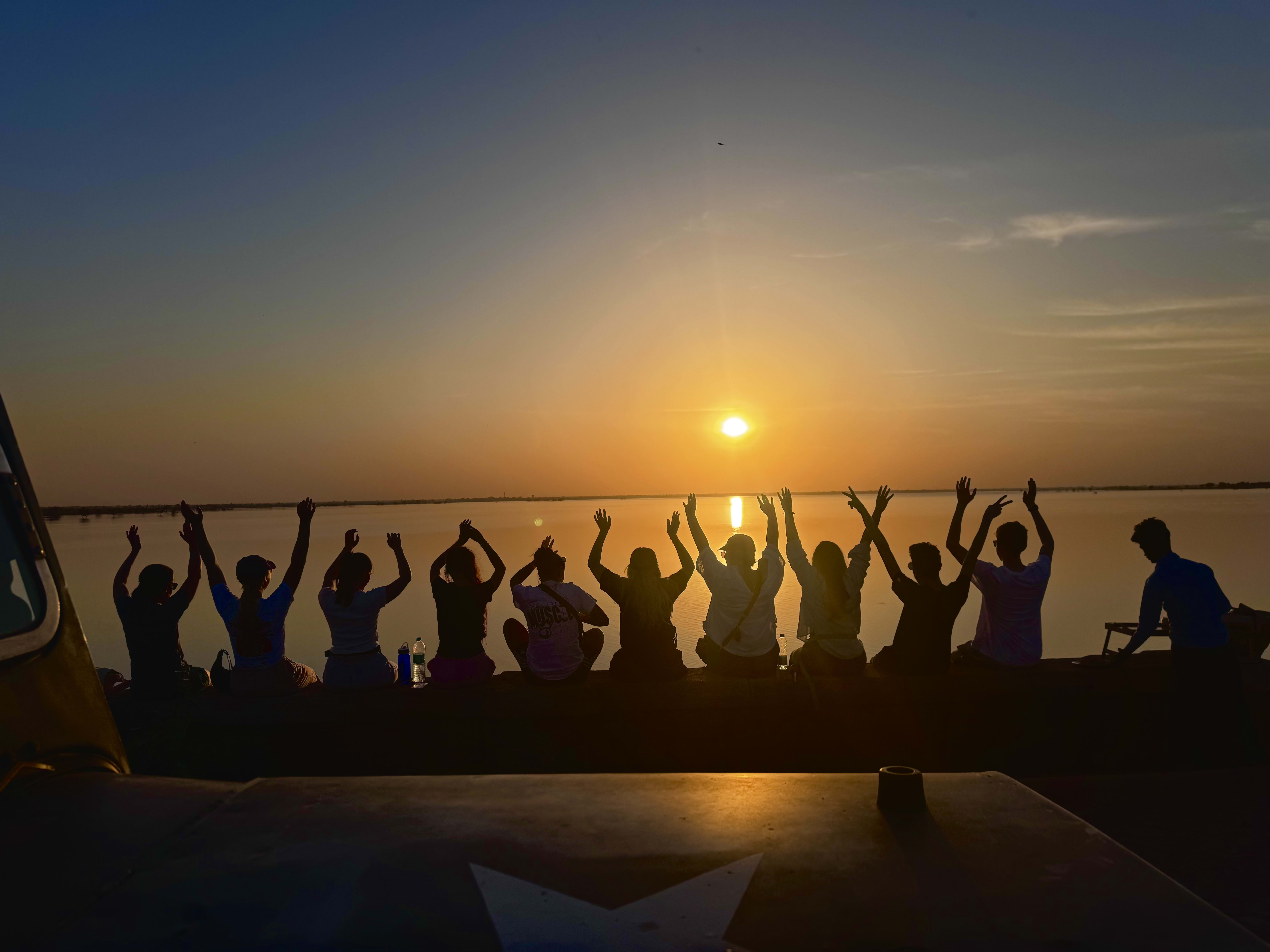 Travellers silhouetted with arms raised at sunset