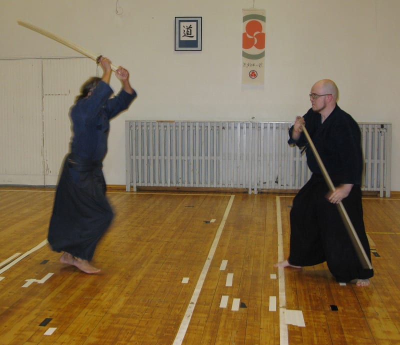 Jōdō-Übung in einer Halle: Links holt ein Übender mit dem hölzernen Schwert über dem Kopf aus, rechts empfängt ihn ein zweiter mit dem diagonal gehaltenen Jō