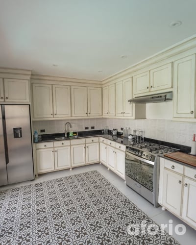 Cocina equipada con muebles color crema, refrigeradora, cocina de seis hornillas y piso de mayólica con diseño geométrico