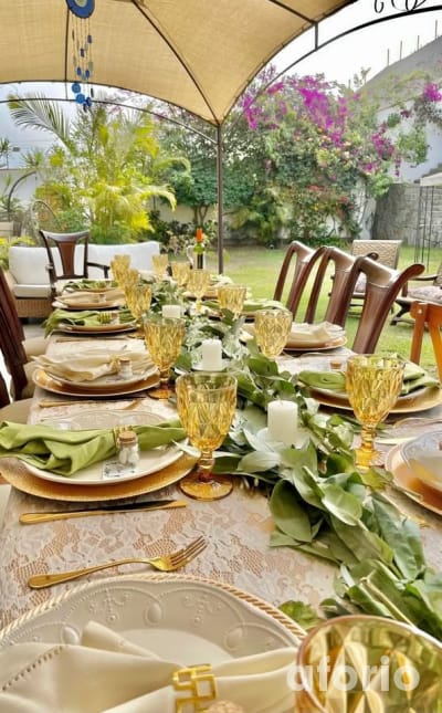 Mesa larga decorada al aire libre con copas amarillas, vajilla dorada y centro de mesa de eucalipto bajo carpa, lista para evento
