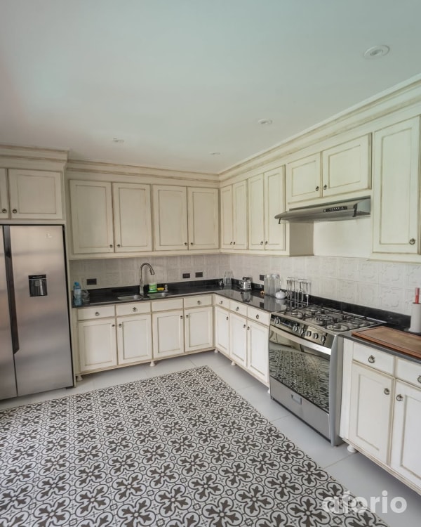 Cocina equipada con muebles color crema, refrigeradora, cocina de seis hornillas y piso de mayólica con diseño geométrico