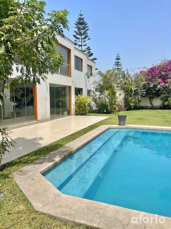Casa moderna de dos pisos en La Molina con piscina rectangular y jardín rodeado de palmeras y buganvillas