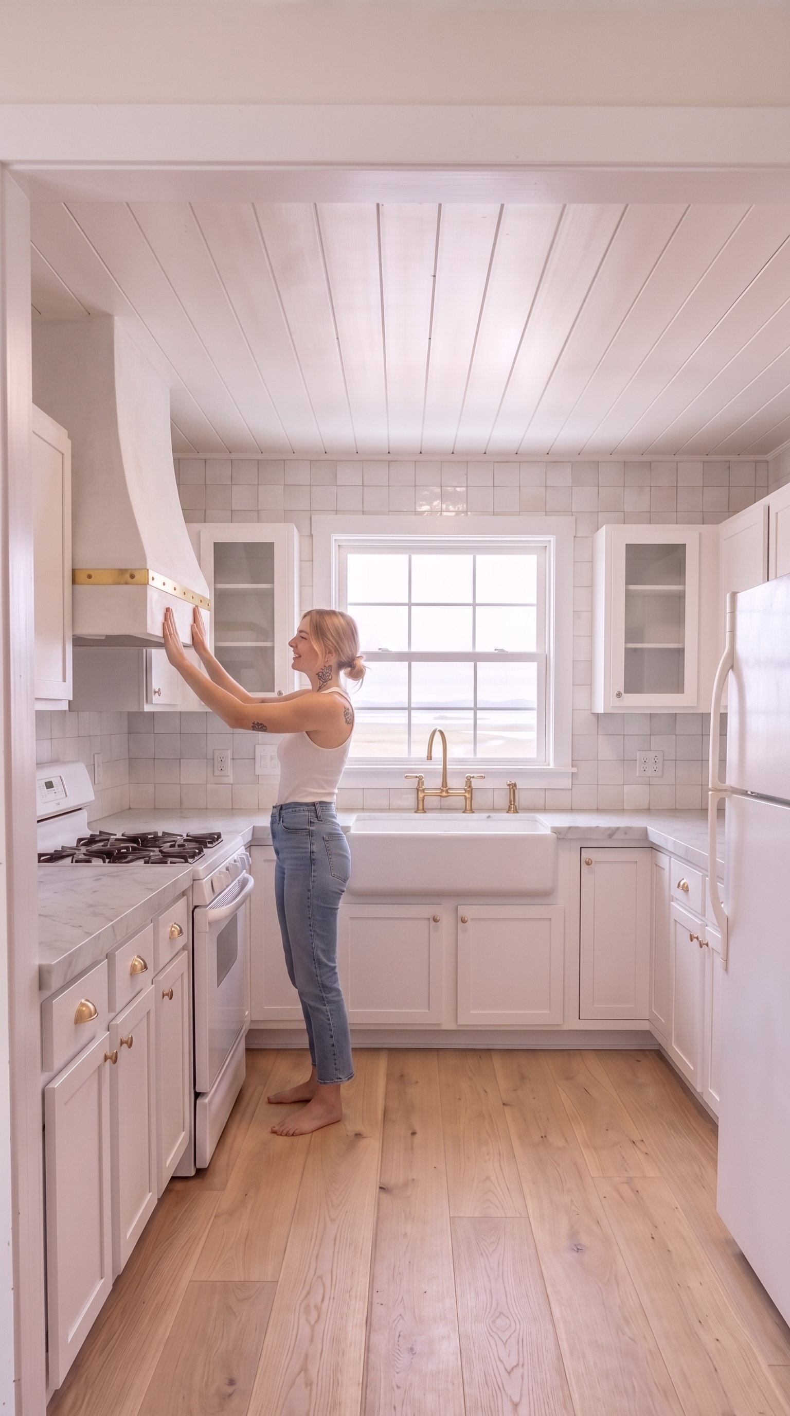 A custom smooth white plaster range hood tapering upward from the LEFT wall directly above the white gas range up into the shiplap ceiling with a single unlacquered-brass band strap wrapped around its base with visible brass rivets
