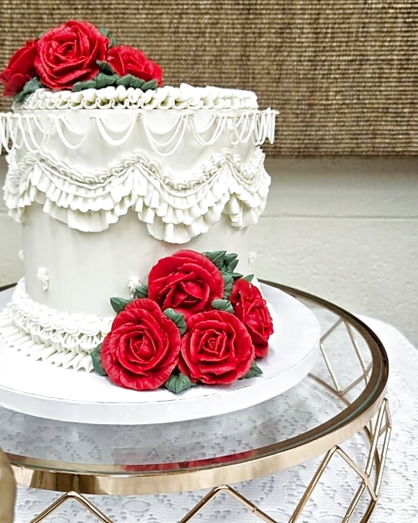 Single-tier white wedding cake crowned with piped red buttercream roses and ruffled vintage piping