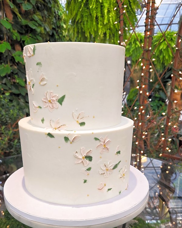 White two-tier wedding cake with blush palette-knife flowers and gold pearl accents
