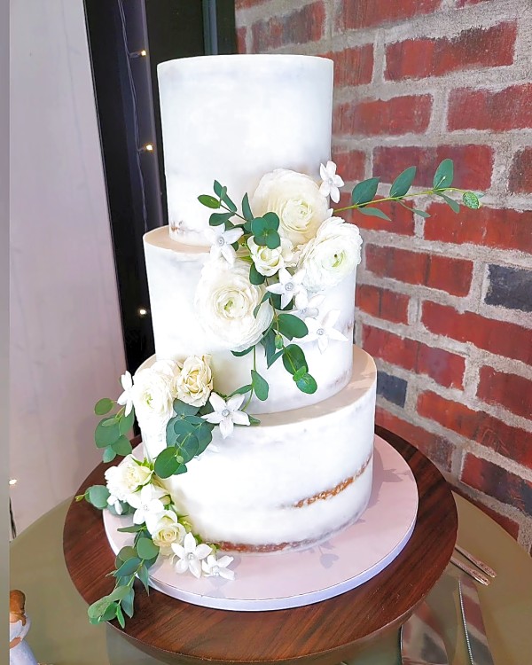 Three-tier semi-naked wedding cake with white roses and greenery at Grove Station