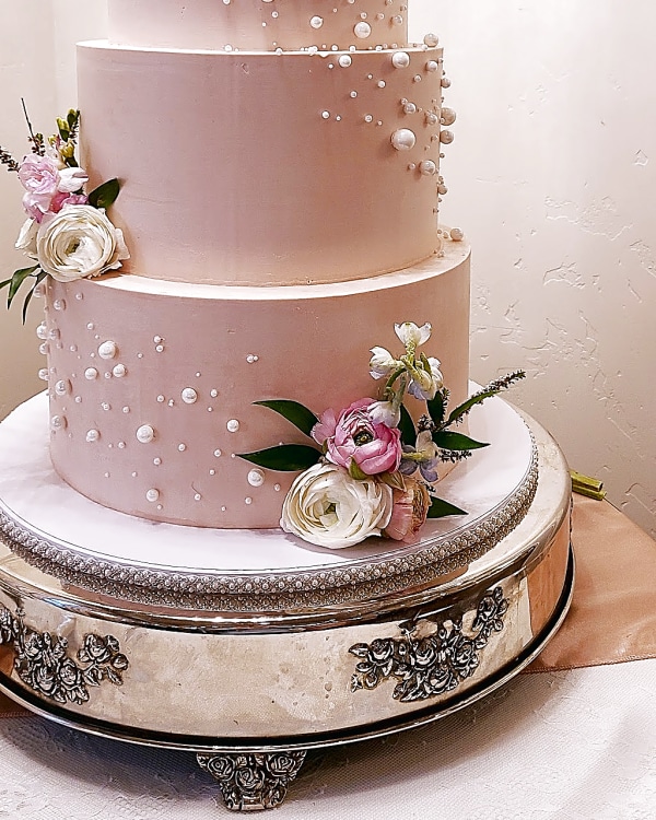 Blush wedding cake with three pale pink tiers, pearl detailing and fresh blooms on a silver pedestal by Sweet E's Bakery