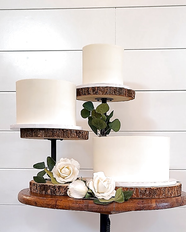 Three individual white wedding cakes on wood slice stands with white roses