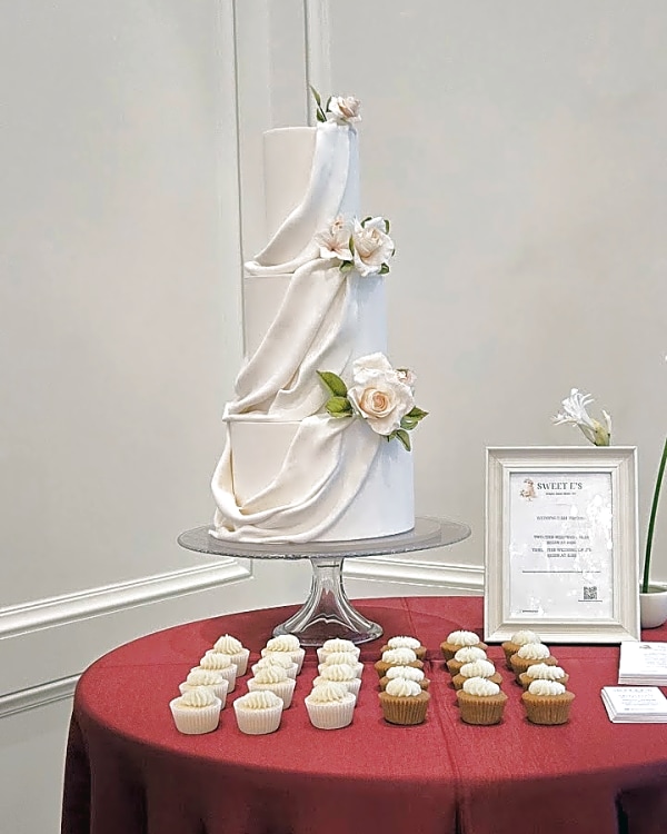 Three-tier white fondant wedding cake with a sweeping drape and blush sugar roses