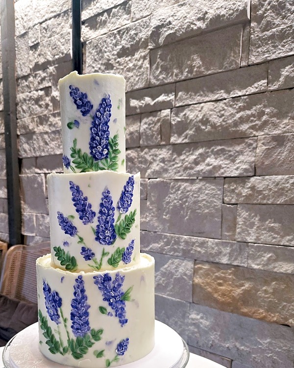 Wedding cake by Sweet E's Bakery in Lindon, a three-tier round cake with white buttercream and purple floral palette knife painting