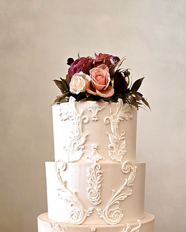 Wedding cake by Sweet E's Bakery in Spanish Fork, three-tier wedding cake with ivory buttercream, white piped rococo-inspired details, and a fresh