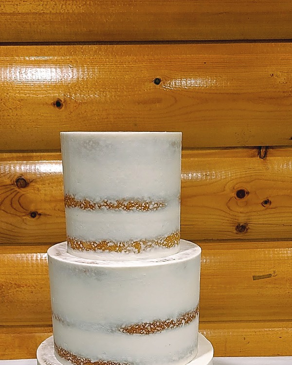 Three-tier semi-naked wedding cake with gold stripes on a wood stand