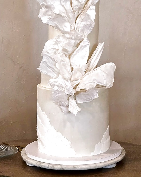 Wedding cake by Sweet E's Bakery in Lindon, a four-tier wedding cake with white buttercream, featuring white edible wafer paper details and