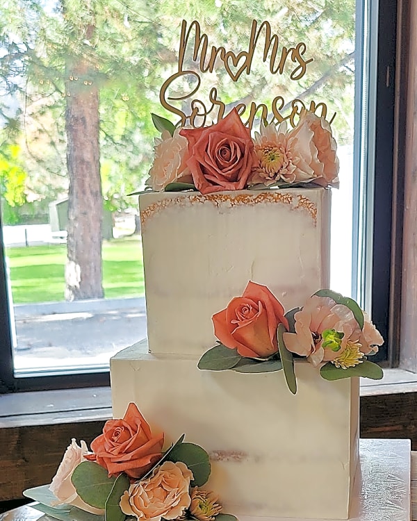Square two-tier semi-naked wedding cake with peach roses and a gold Mr and Mrs topper