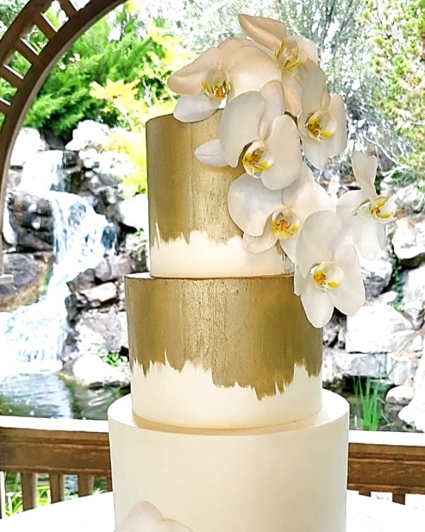 Gold wedding cakes by Sweet E's Bakery: hand-painted gold tiers with a cascade of white orchids at Hidden Falls, Utah