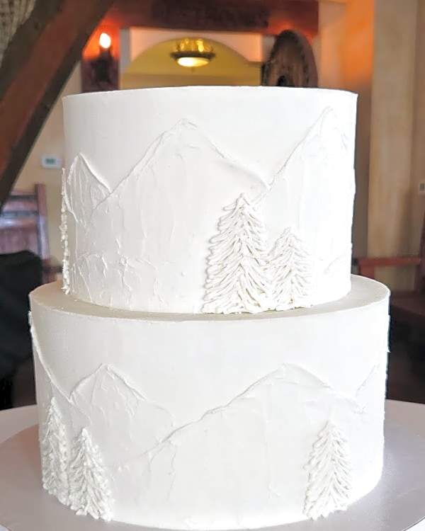 Wedding cake by Sweet E's Bakery in Lindon, two-tier white buttercream cake with textured mountain and piped pine tree details
