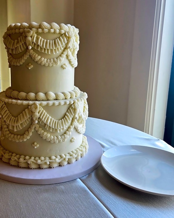 Wedding cake by Sweet E's Bakery in Draper, two-tier buttercream cake in ivory with piped swags and rosettes