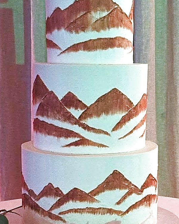 Wedding cake by Sweet E's Bakery in Sundance, a three-tier white wedding cake with brushed copper mountain peaks and a base of white roses and