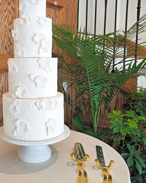 Wedding cake by Sweet E's Bakery in Mapleton, four-tier round white wedding cake with white lace floral appliqué and texture