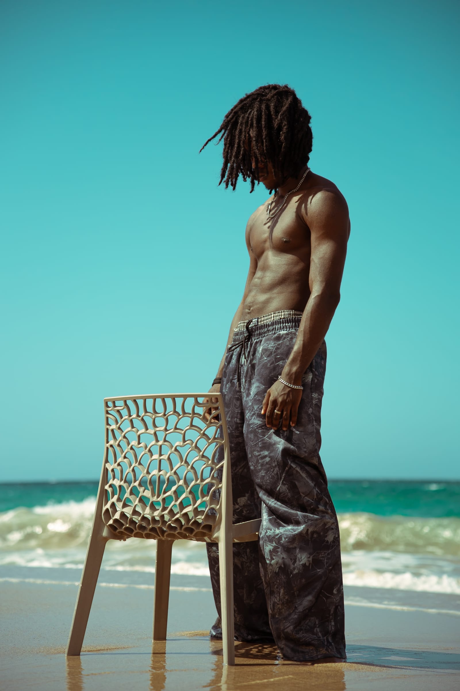 Mathys debout a cote d'une chaise sur le sable, mer et ciel bleus