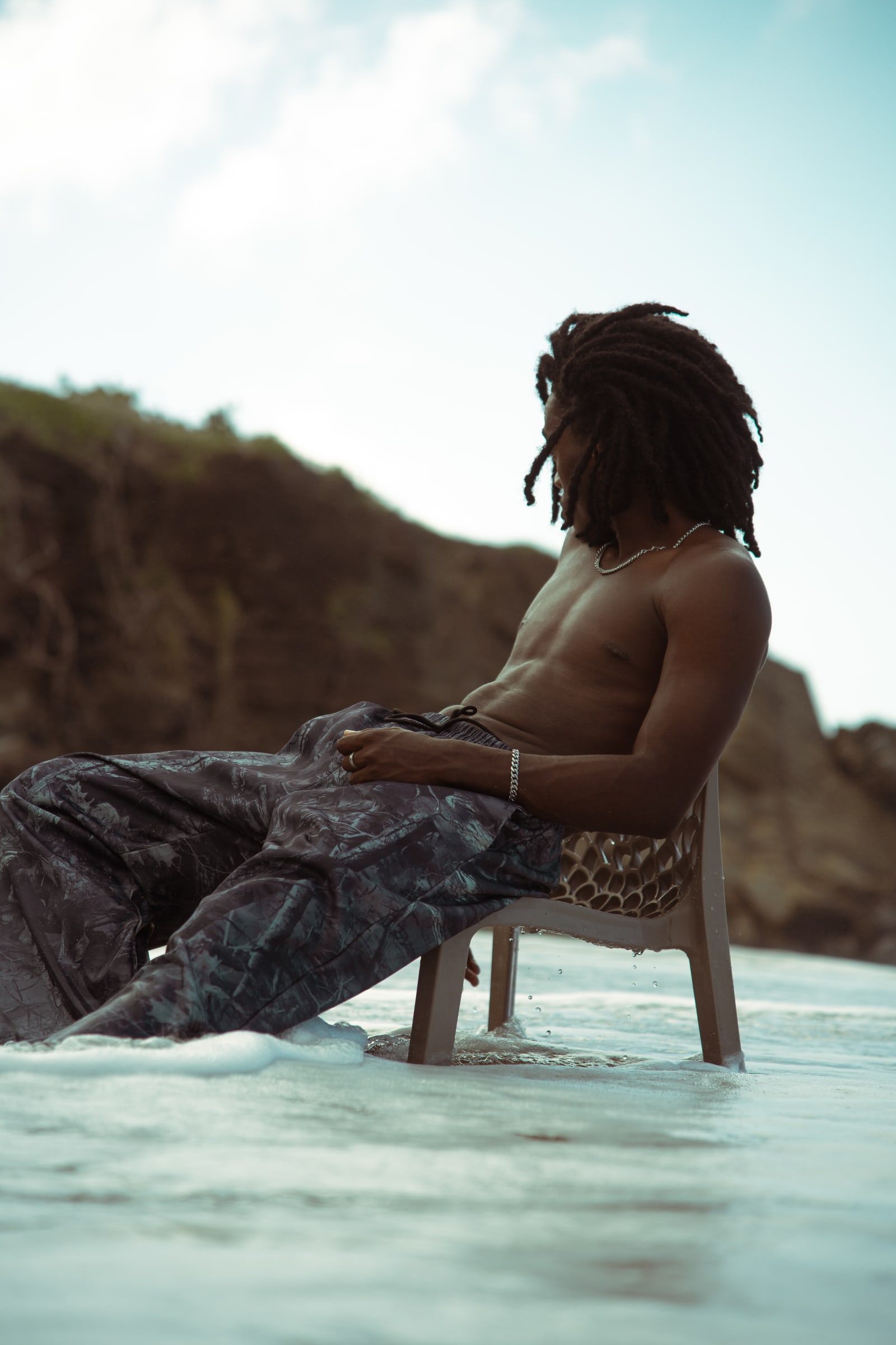 Mathys assis sur une chaise au bord de l'eau, falaise en arriere-plan