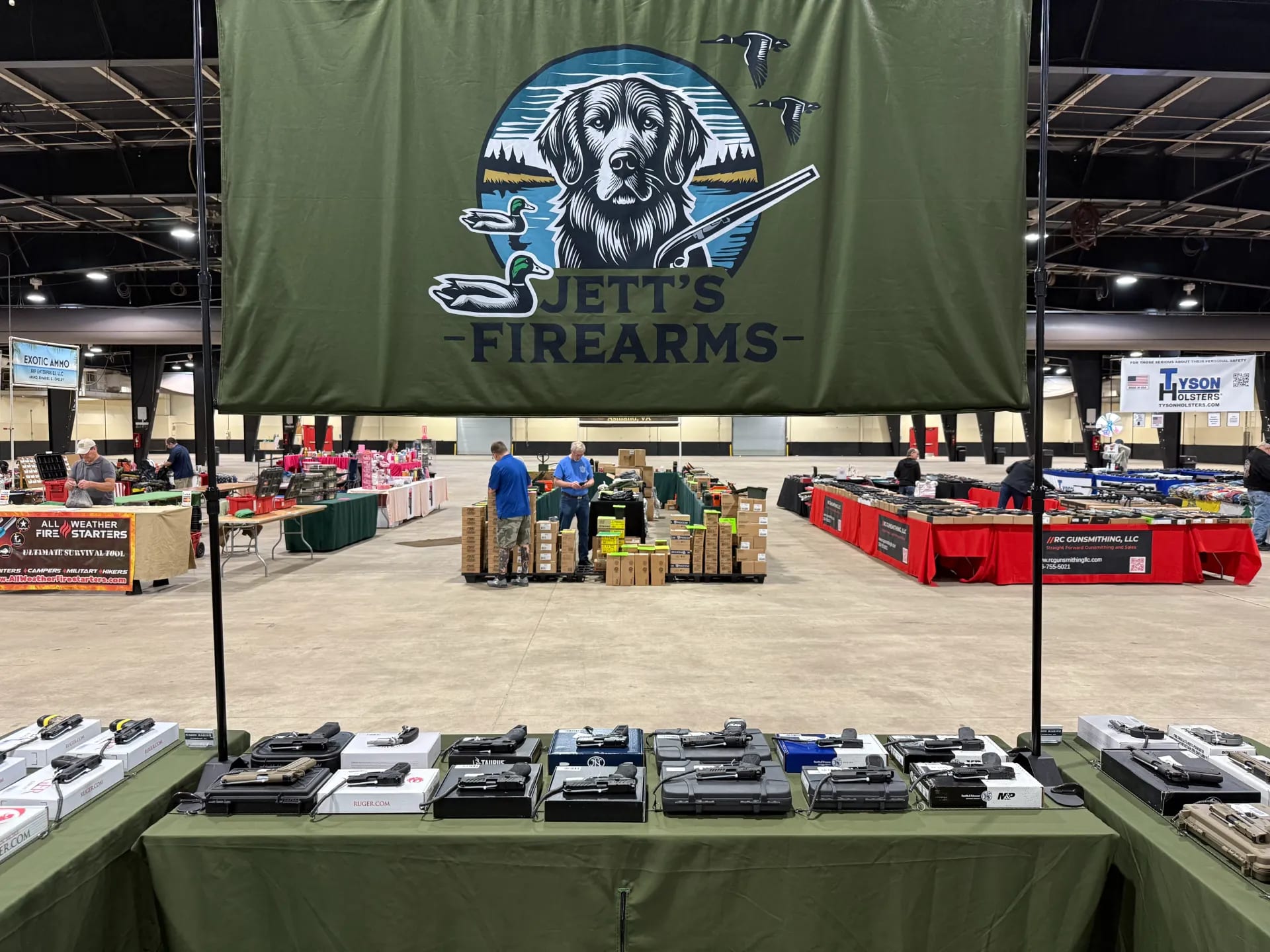 Jett's Firearms gun show vendor table in North Carolina — green branded tablecloth and banner displaying handguns, rifles, and firearms for sale