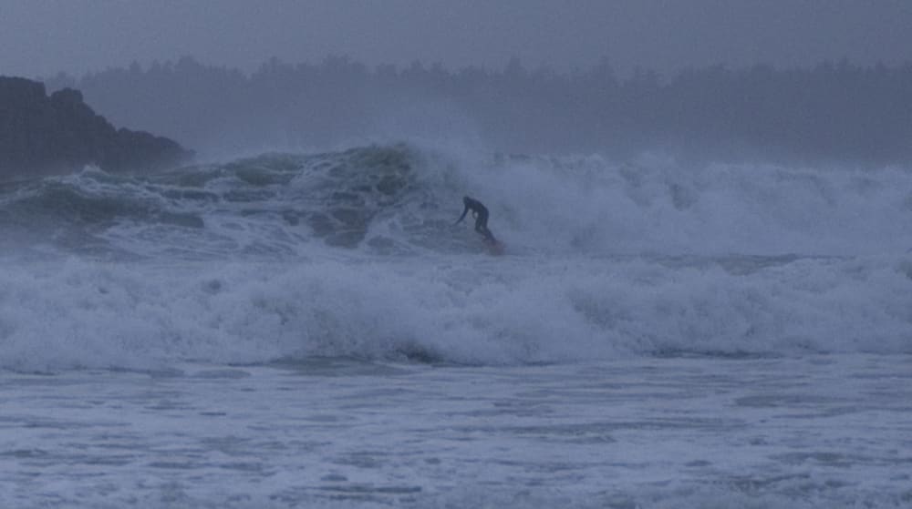 A lone surfer dropping into heavy grey winter surf near Tofino